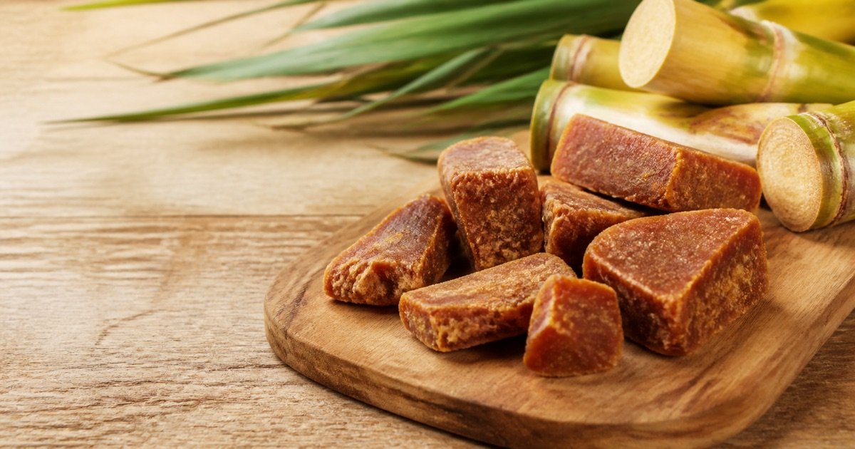 Pedaços de rapadura ao lado de cana-de-açúcar sobre uma tábua de madeira